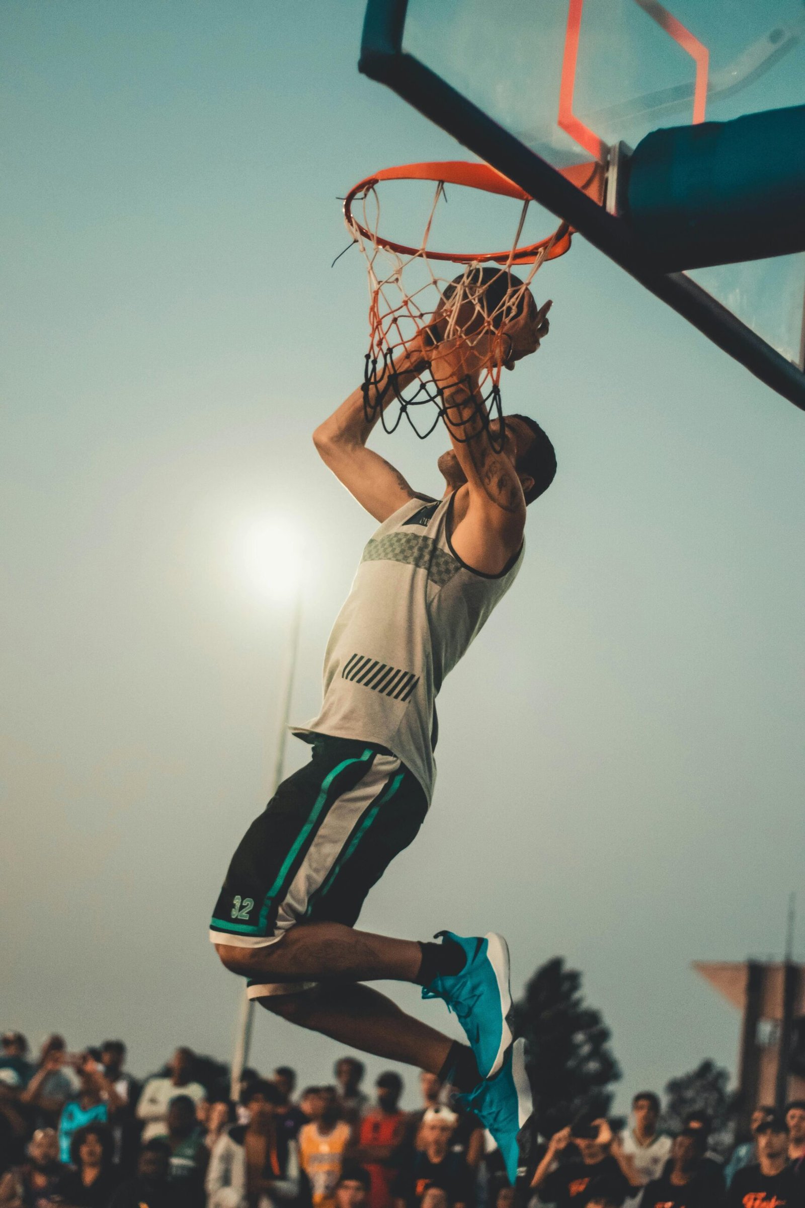 Athlete performs a powerful dunk on an outdoor basketball court at dusk.