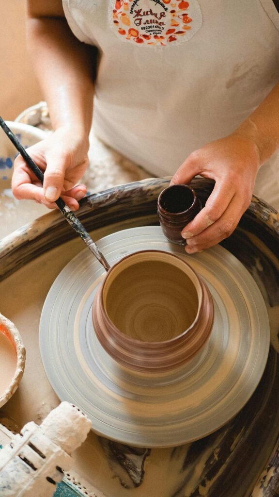 Detailed view of a potter's hands shaping pottery with a paintbrush and pottery wheel.